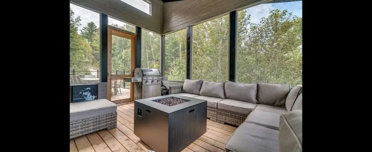 Una zona de estar cubierta tiene un sofá seccional y una mesa cuadrada con fogón.
