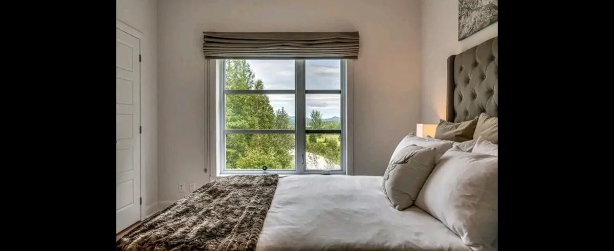 Un dormitorio con una ventana grande con vistas a árboles verdes.
