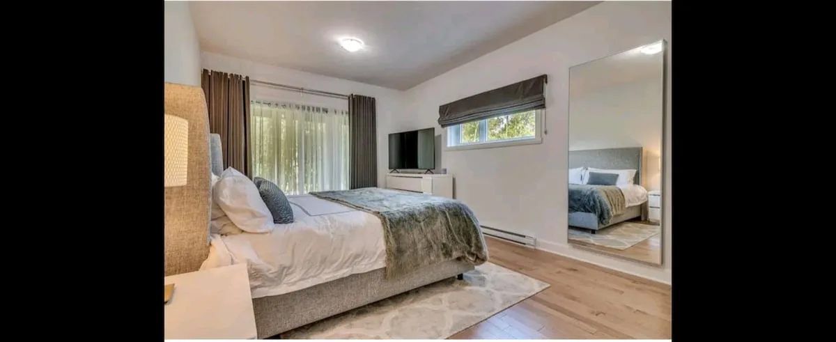 Un dormitorio con una cama, una ventana con cortinas y un televisor en la pared.