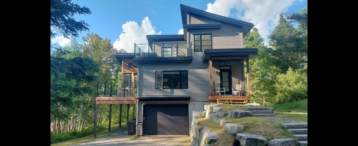 Una casa moderna se alza entre árboles, con una entrada que conduce al garaje.