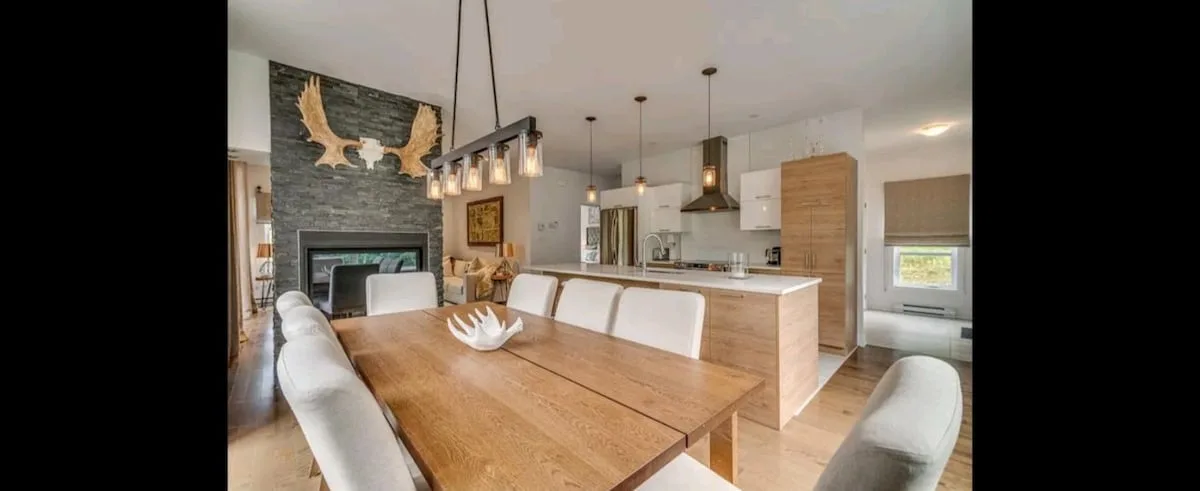 Una cocina abierta con comedor, mesa de madera y lámparas colgantes.