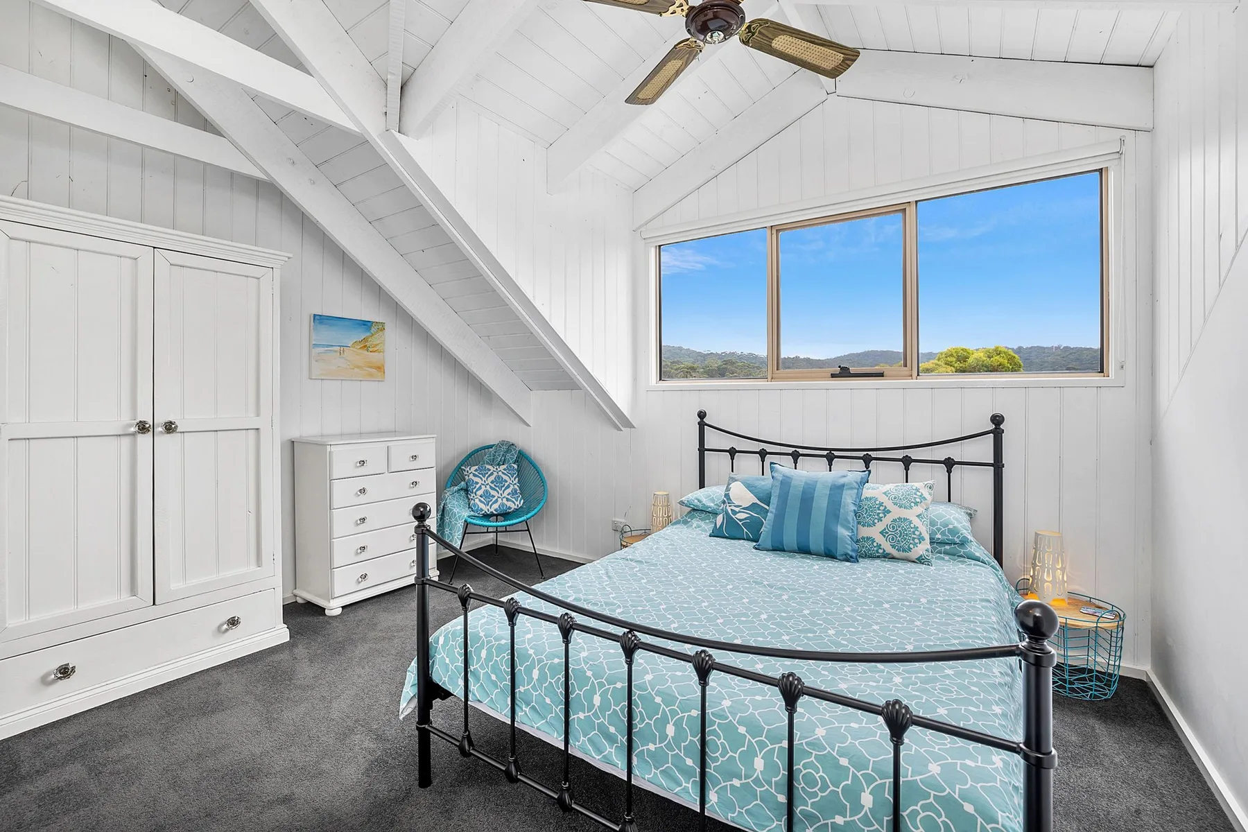 Un dormitorio con una cama bajo una ventana amplia y un techo blanco inclinado.