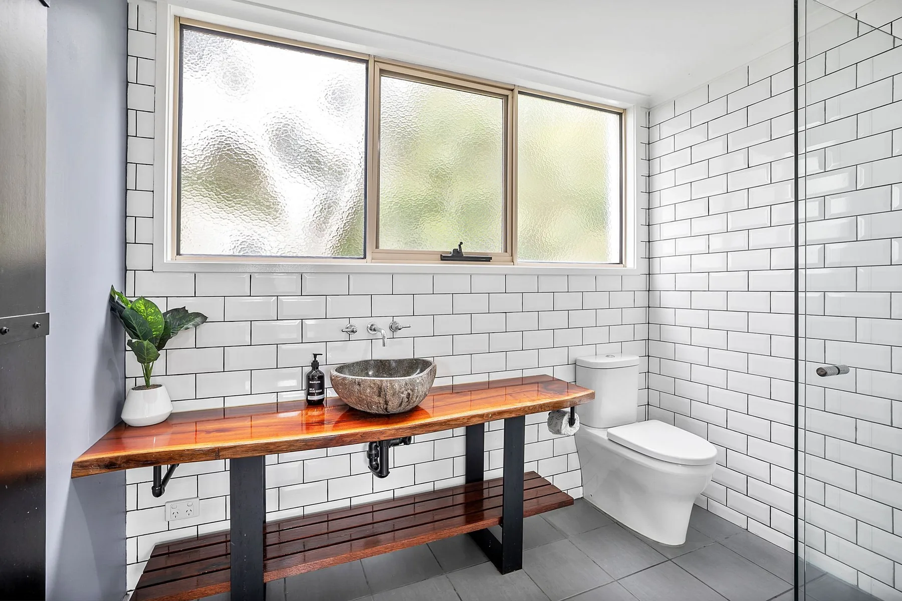 Un baño alicatado con un largo tocador de madera y un inodoro al lado.