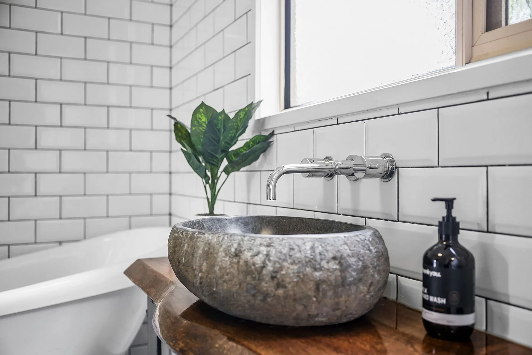 Un tocador de baño con un lavabo de piedra bajo una ventana luminosa.