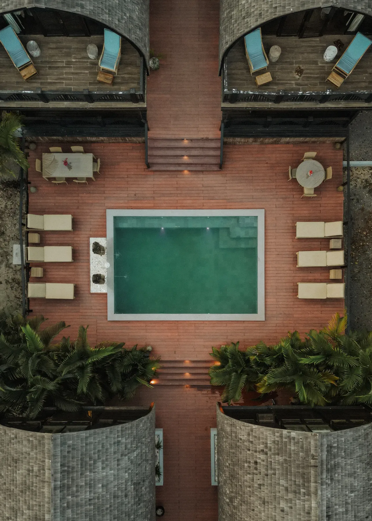 Zona común: Una piscina rectangular ocupa un patio de ladrillo rodeado de tumbonas, mesas y plantas.