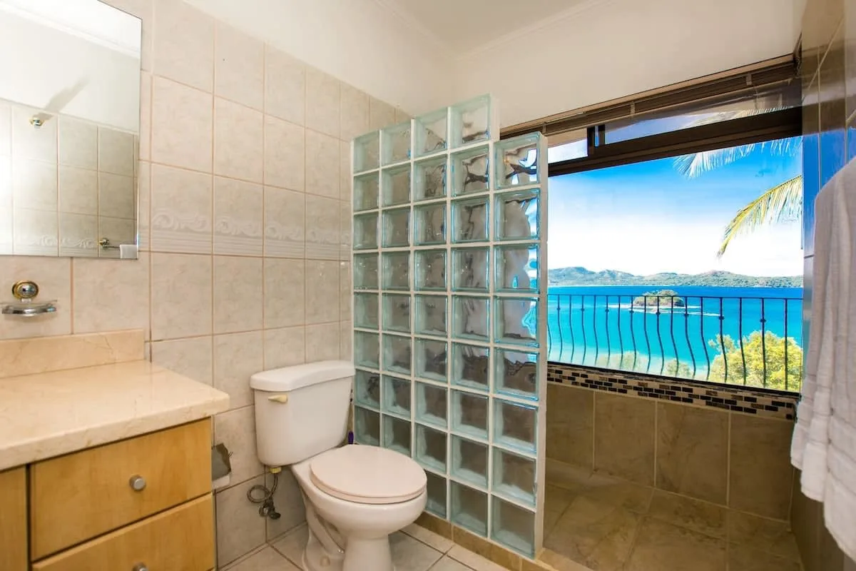 A bathroom with a glass-block partition opens onto a balcony overlooking the sea.