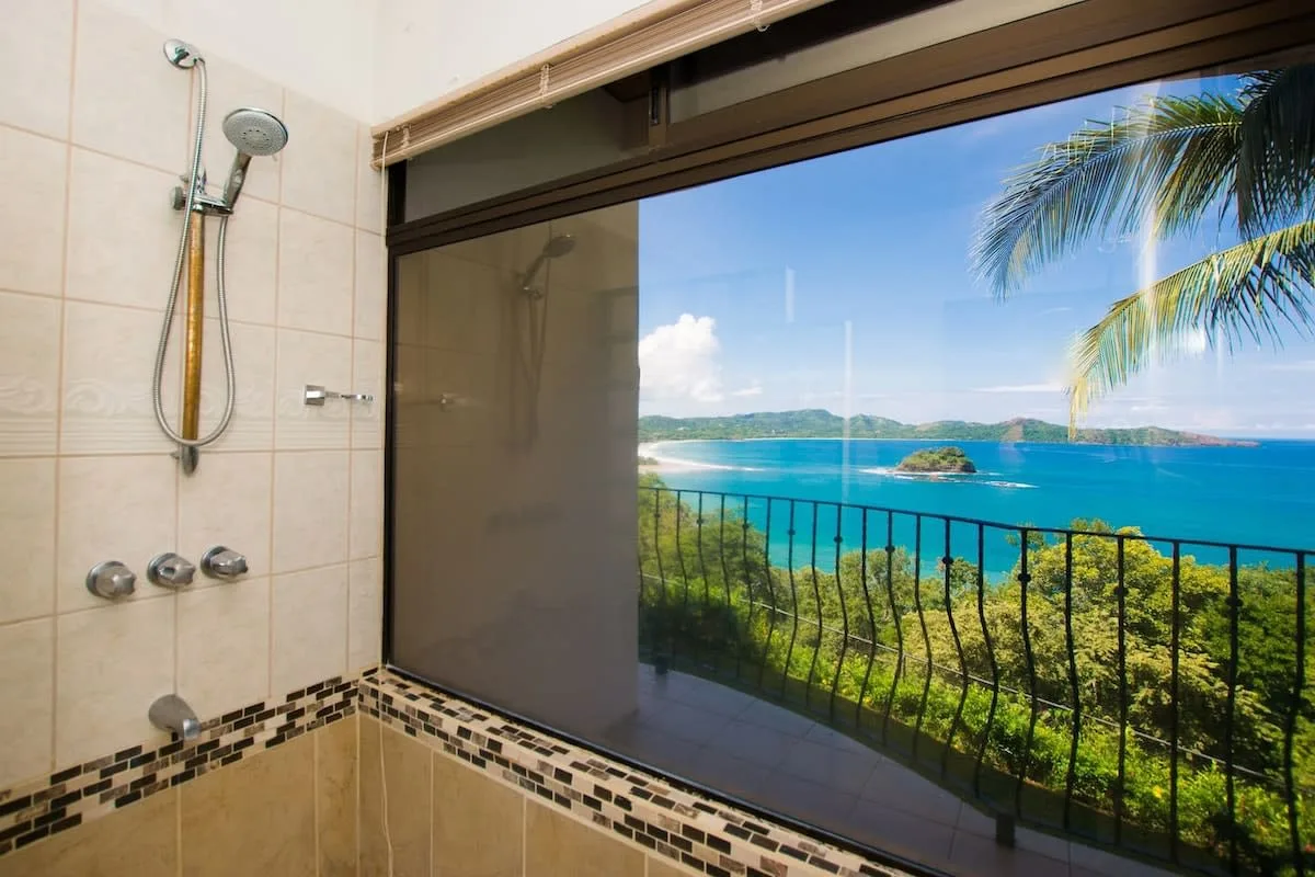 A bathroom shower opens onto a balcony with a view of turquoise water and green islands.