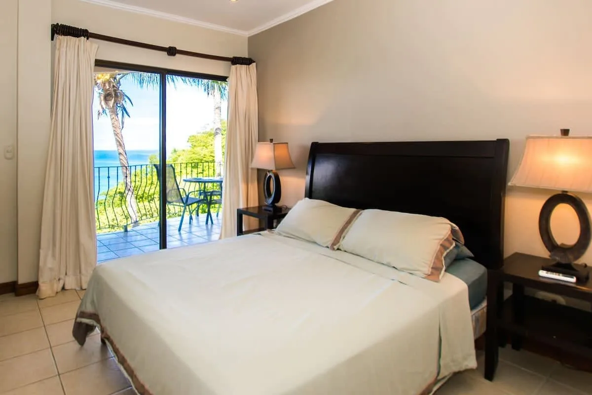 A bedroom with a neatly made bed beside a bright balcony window.