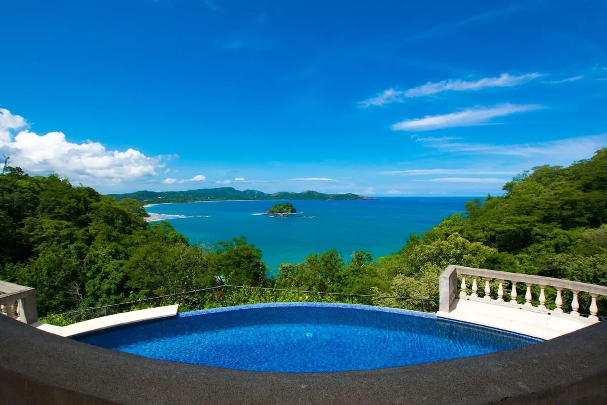 Shared amenity: A swimming pool overlooks a turquoise bay framed by green hills.