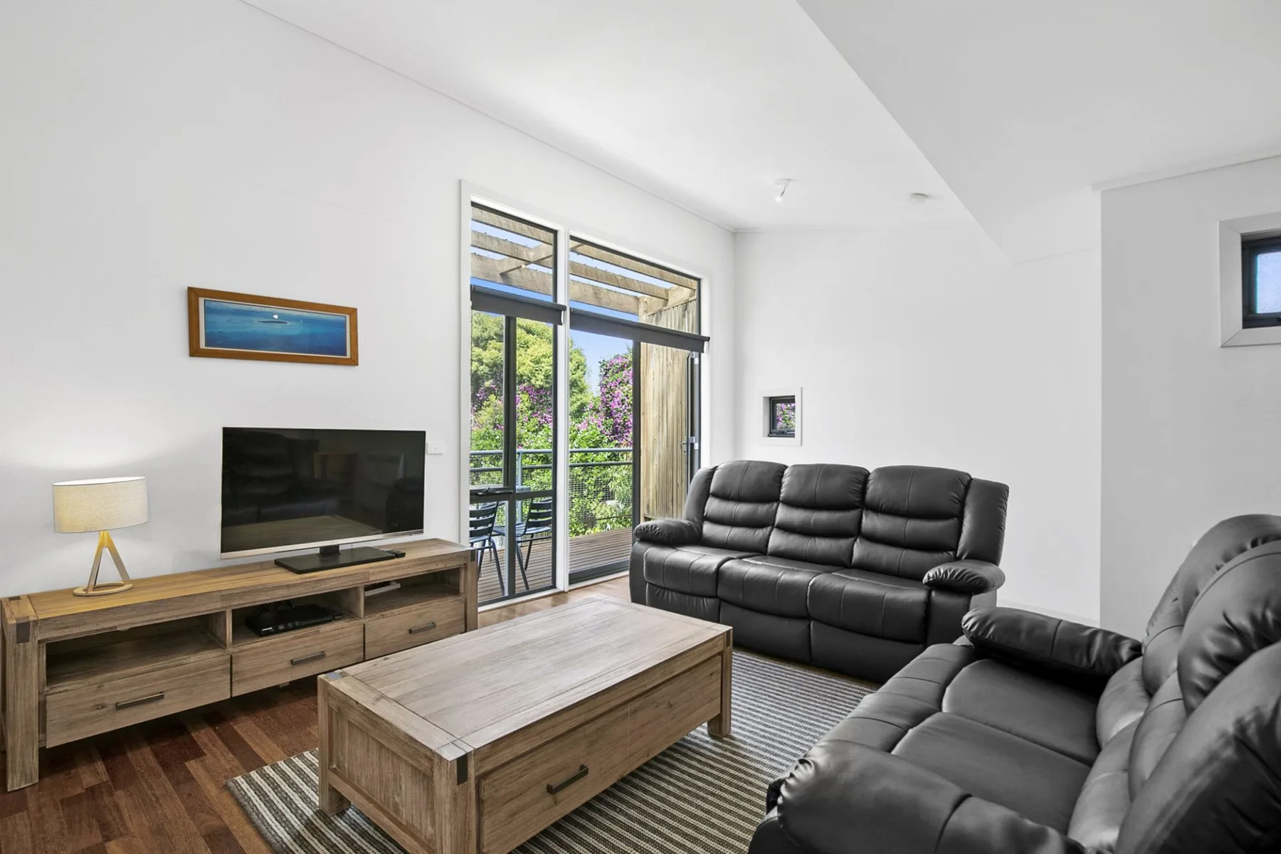 Una sala luminosa con asientos oscuros, una mesa de centro de madera y ventanas grandes.