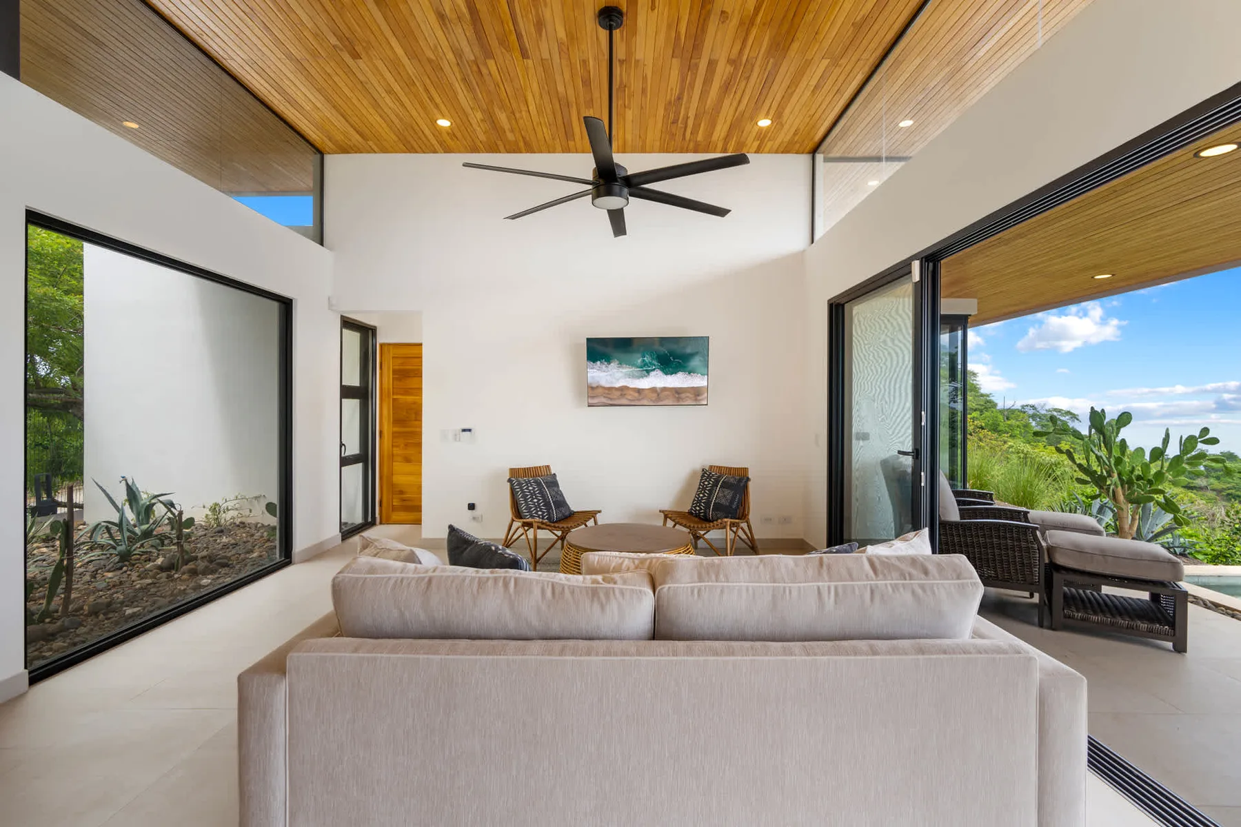A bright living room with seating beneath a wood-paneled ceiling and large windows.