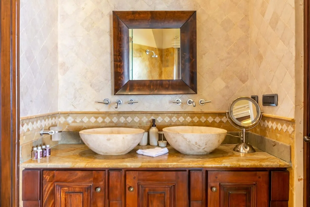A bathroom vanity with two basins, a large mirror, and wooden cabinetry.