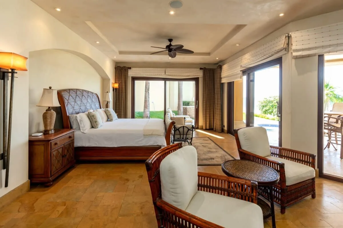 A bedroom with a bed and a small seating area beside large windows.