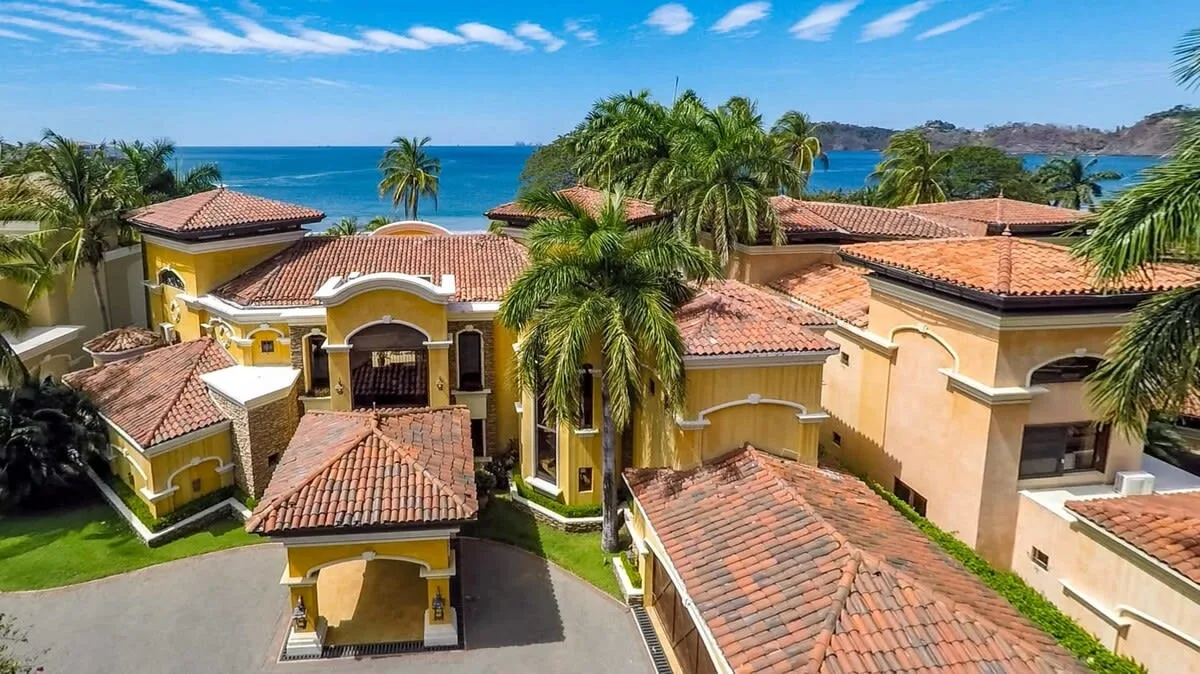 Aerial view of a yellow villa complex with red-tiled roofs and palm trees.