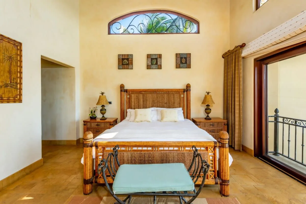 A bedroom with a carved wooden bed and a large arched window.