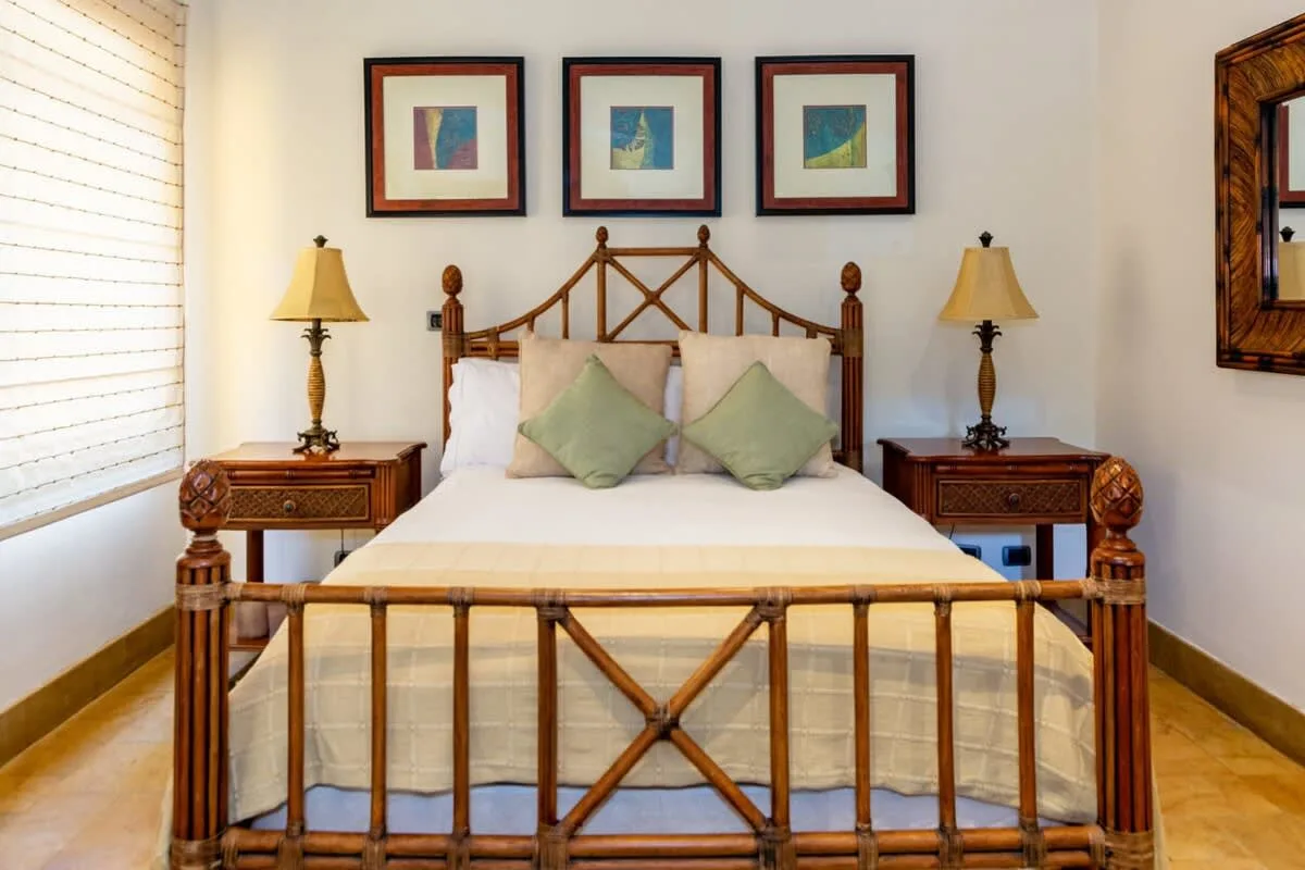 A bedroom with a wooden bed, pale bedding, and framed artwork above it.