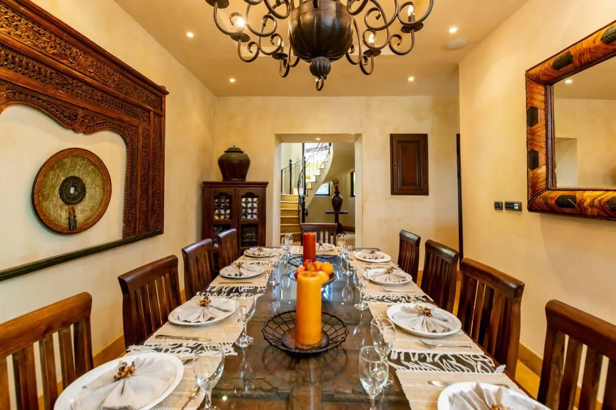 A dining room with a long table set with plates beneath a chandelier.