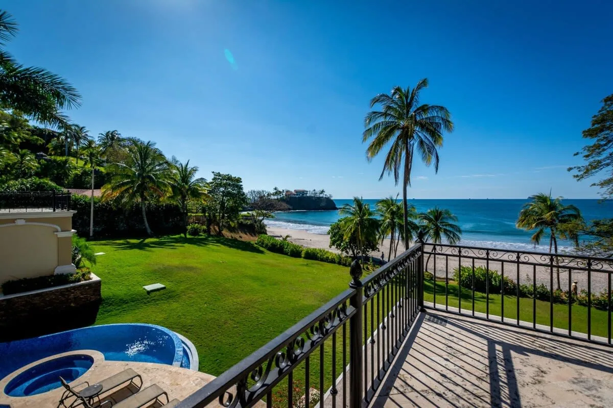 A seaside terrace overlooks a green lawn, palm trees, and the ocean.