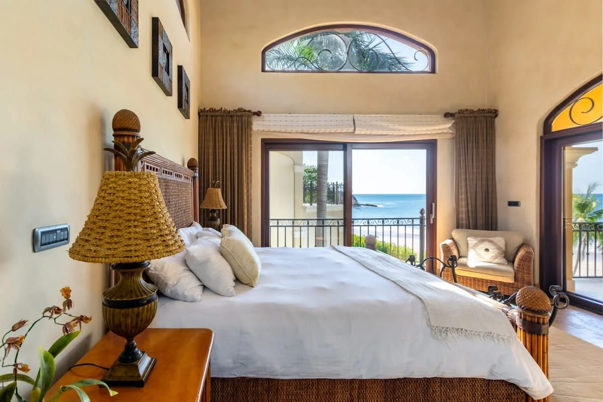 A bedroom with a large bed facing glass doors that open onto a balcony overlooking the sea.