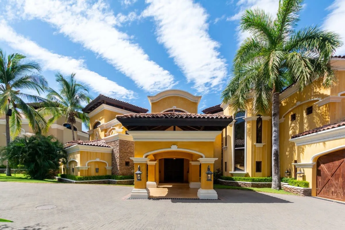 A yellow stucco building faces a paved driveway, with palm trees around the entrance.