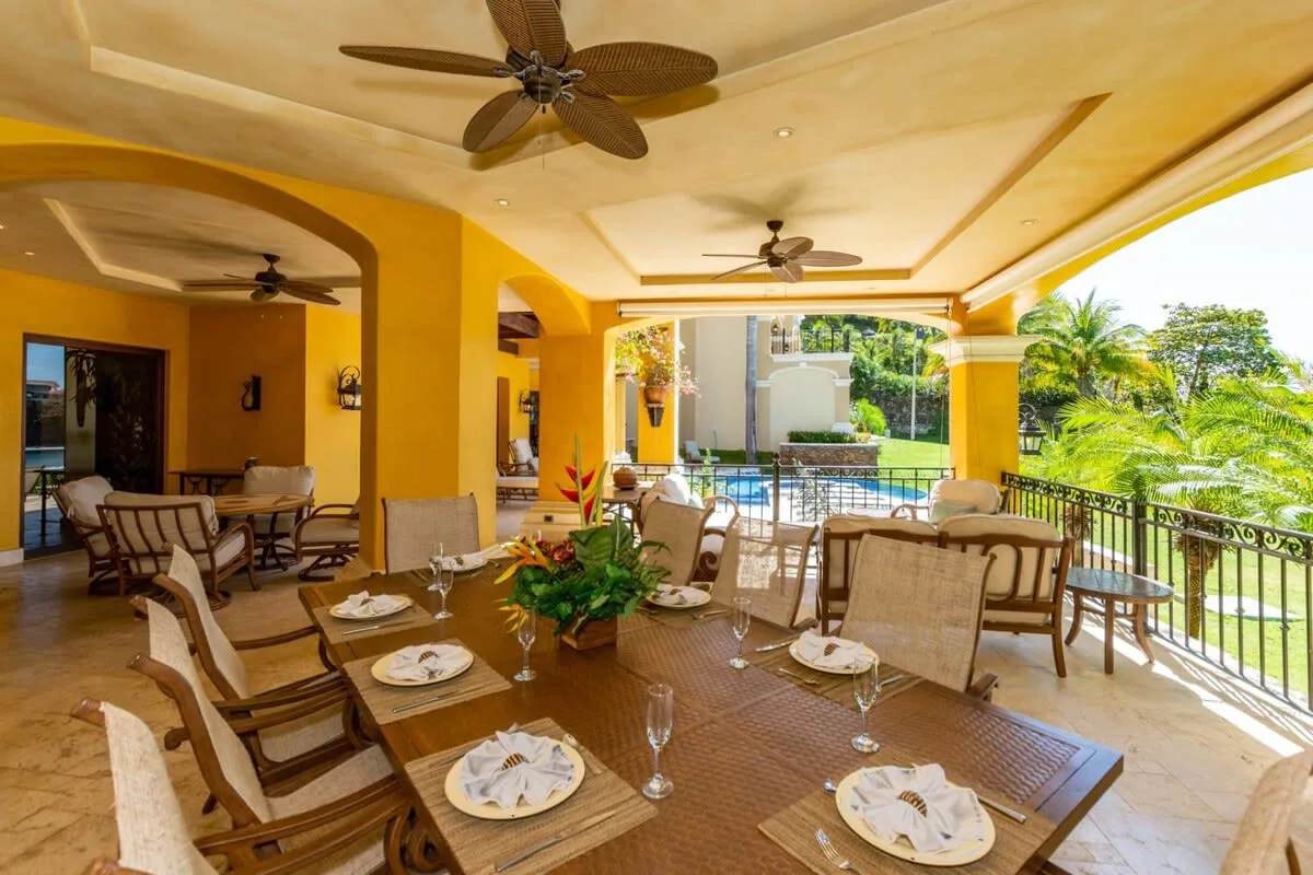 A covered outdoor dining area with tables, seating, and a view of the garden.