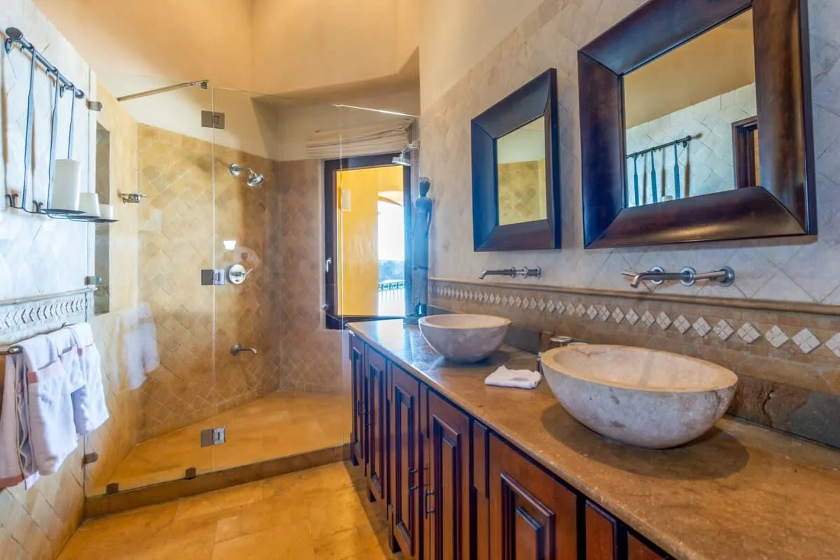A bathroom with a glass shower, double sinks, and large wall mirrors.