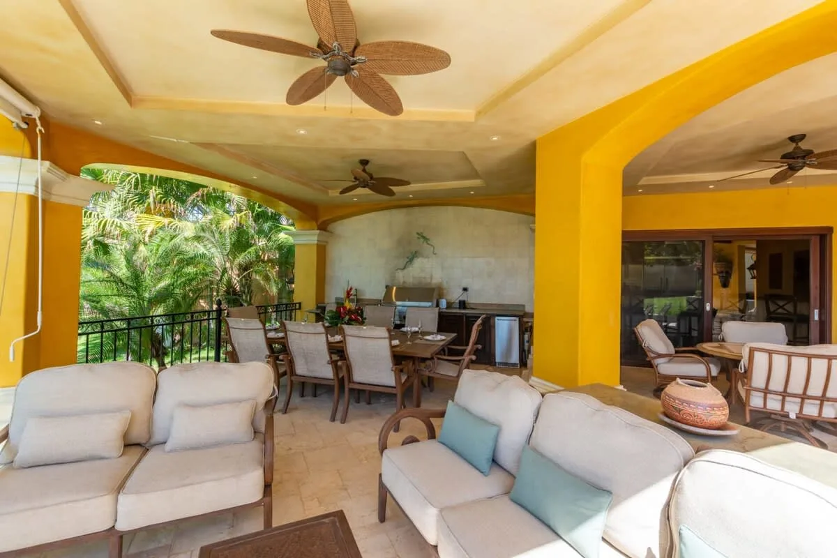 A covered patio seating area with cushioned sofas and a dining table.