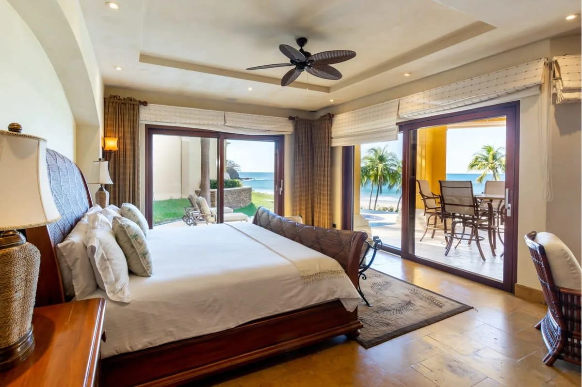 A bedroom opens onto a patio with outdoor seating and palm trees.