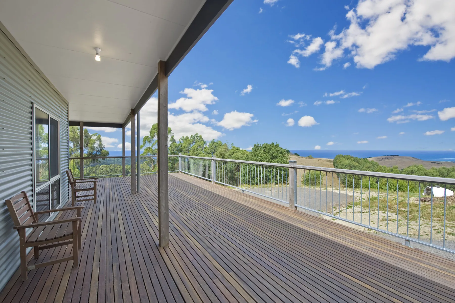 Una terraza exterior cubierta con asientos de madera ofrece vistas a la vegetación y al mar.