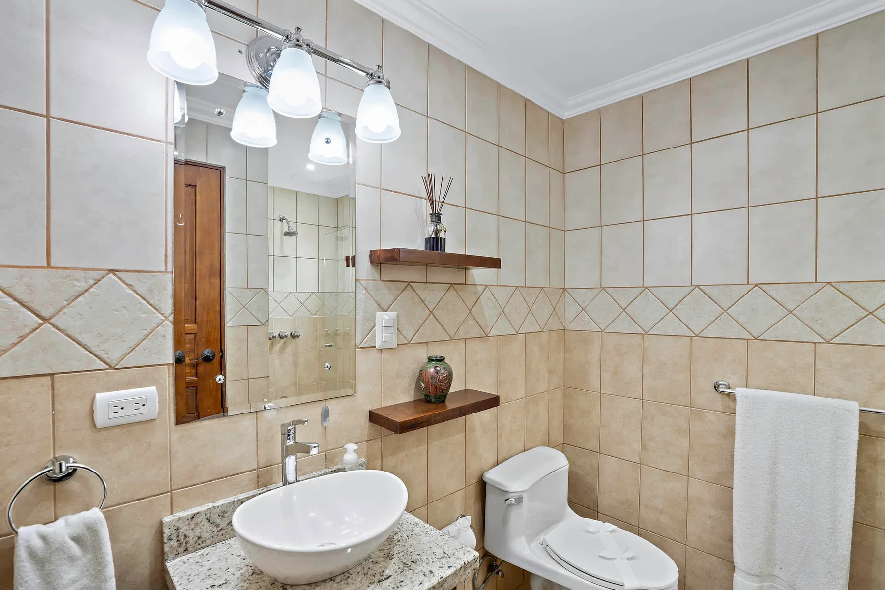 A tiled bathroom with a sink, mirror, and toilet.