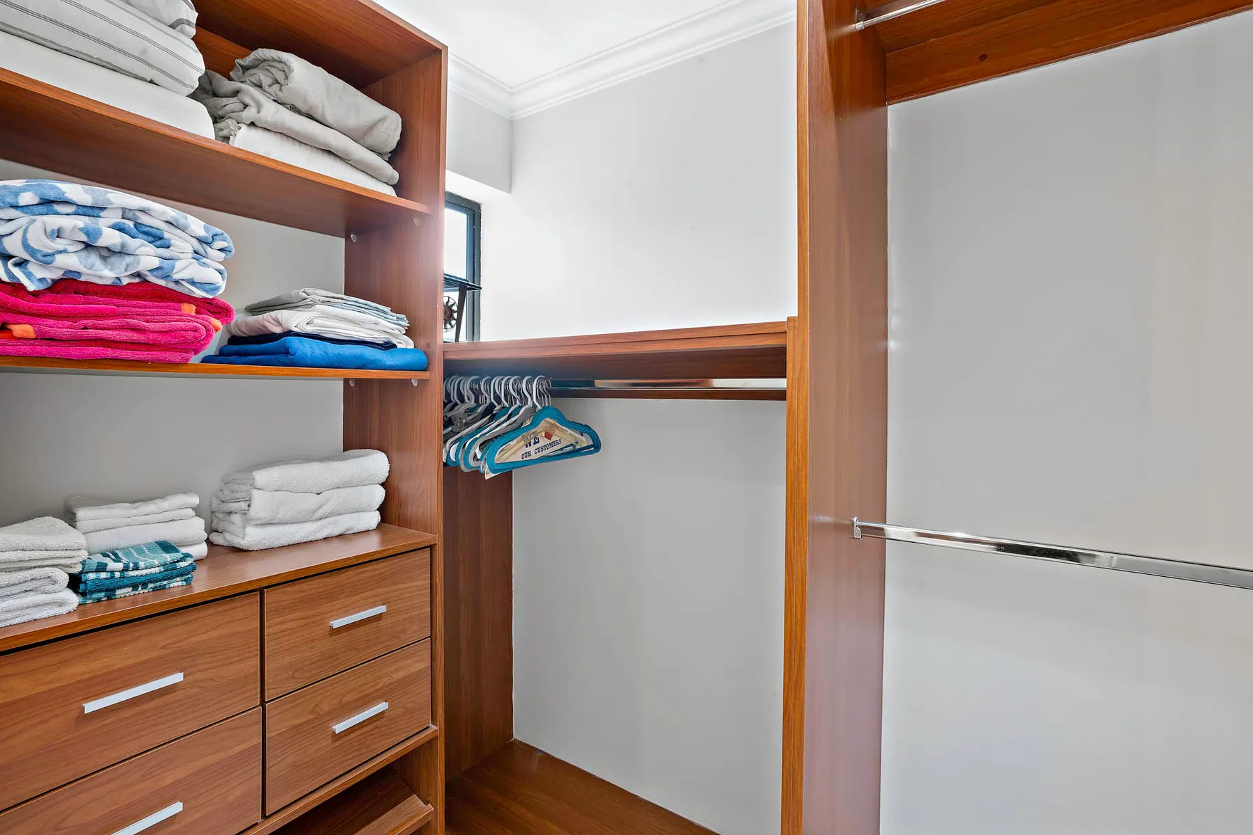 A walk-in closet with wooden shelving, folded linens, and hanging clothes.