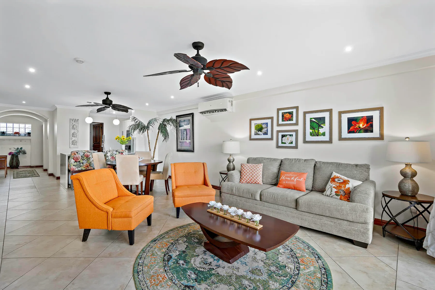 A bright living room with gray seating, orange armchairs, and framed artwork.