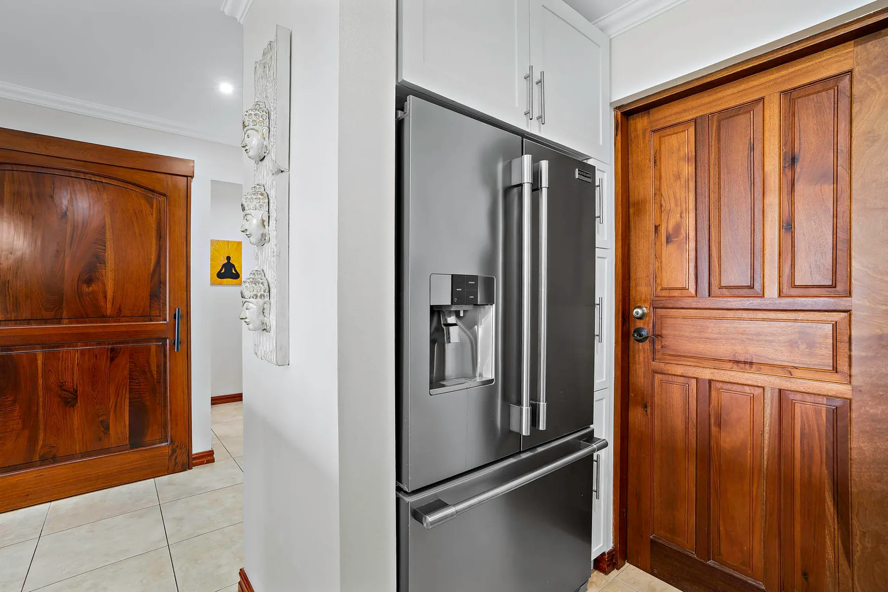 A kitchen refrigerator stands between two wooden doors.