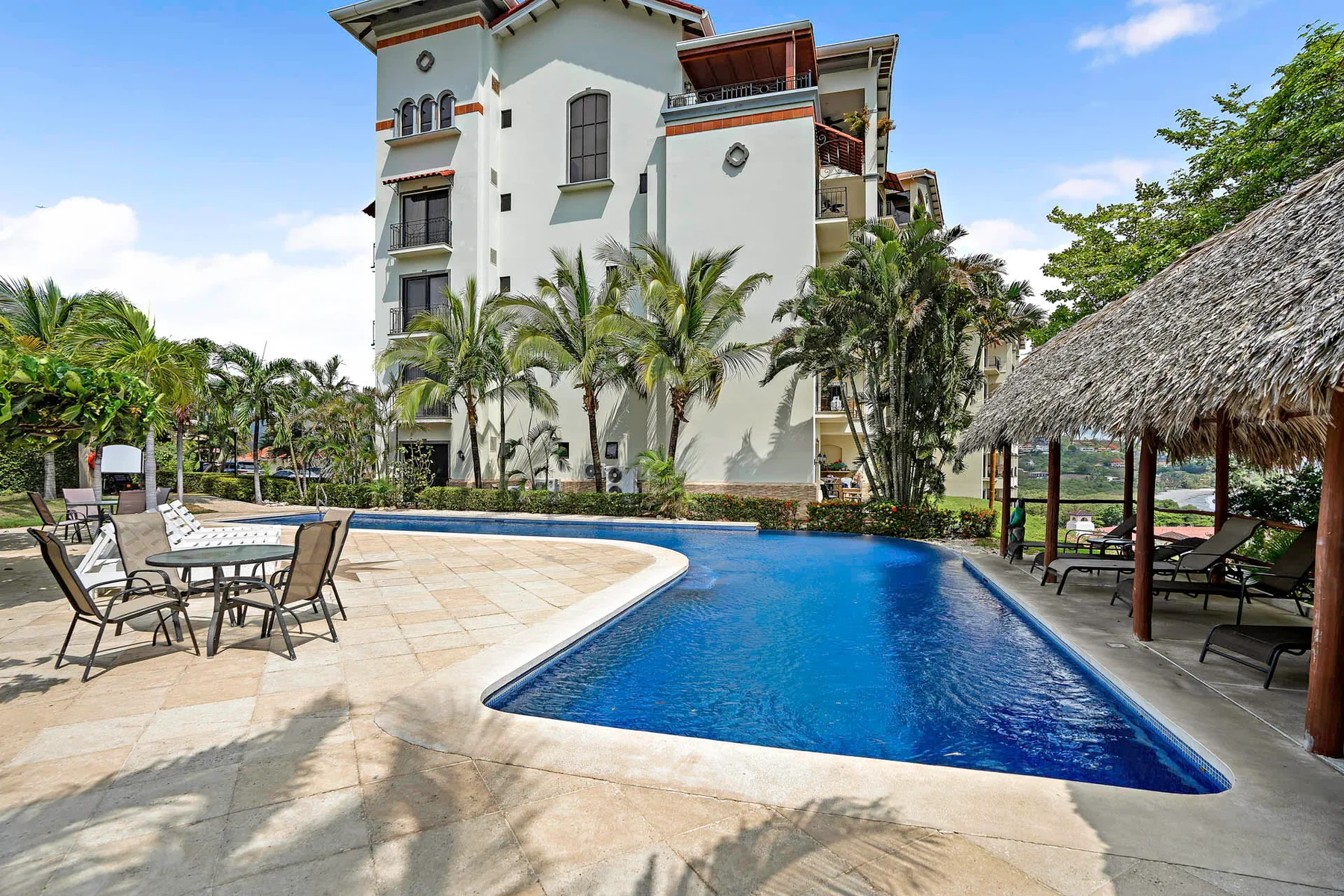 Shared amenity: An outdoor swimming pool sits beside a white multi-story building and palm trees.