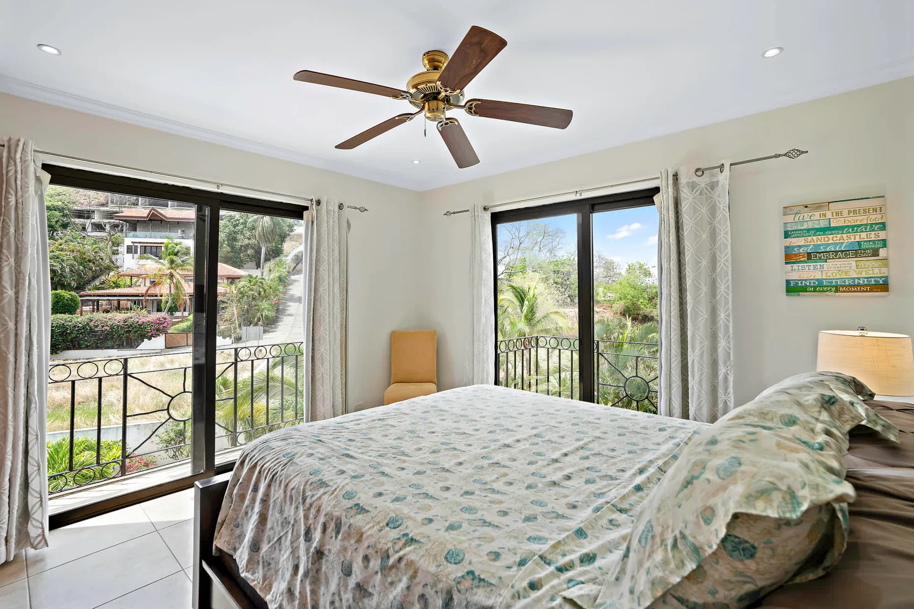 A bedroom with a bed beside large windows overlooking greenery.