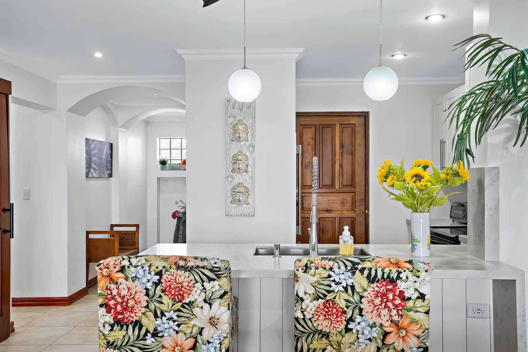 A bright kitchen with a central island, floral seating, and fresh flowers.