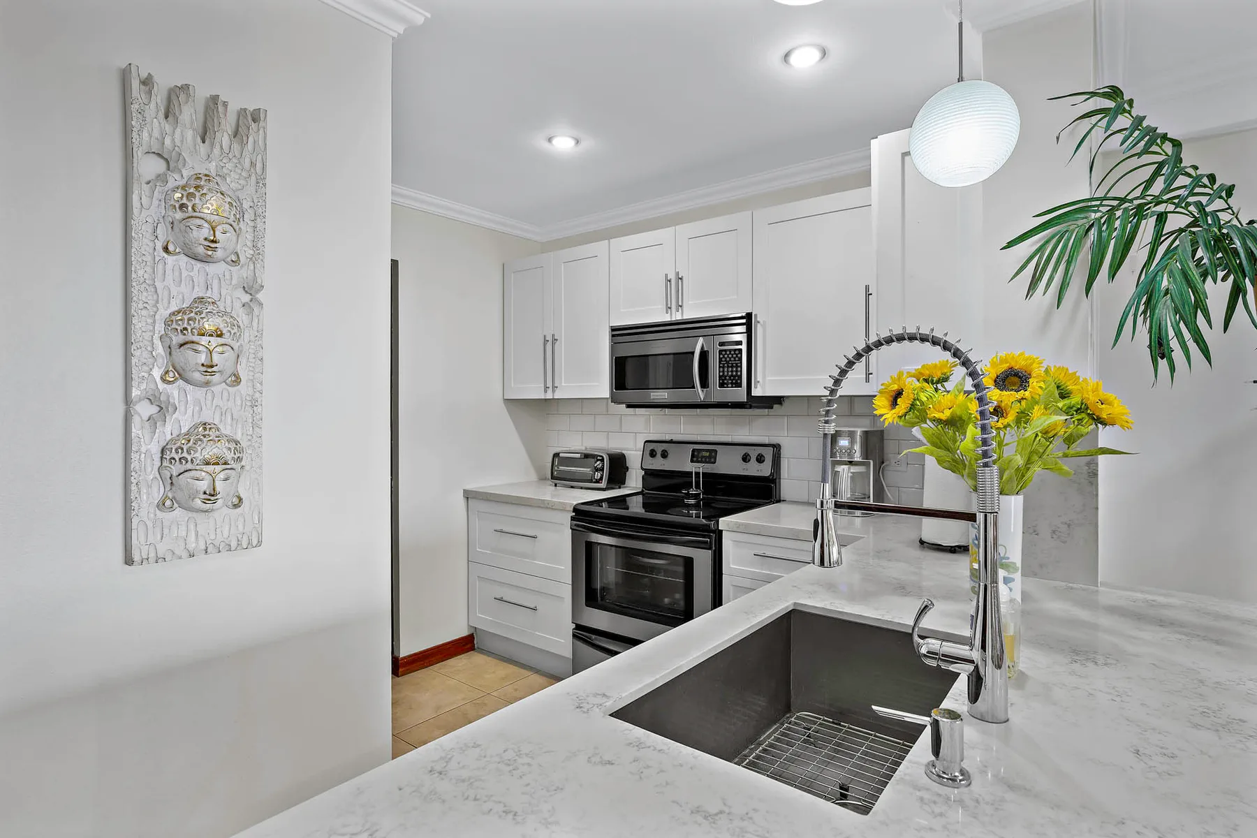 A bright kitchen with white cabinets, stainless steel appliances, and a large sink.