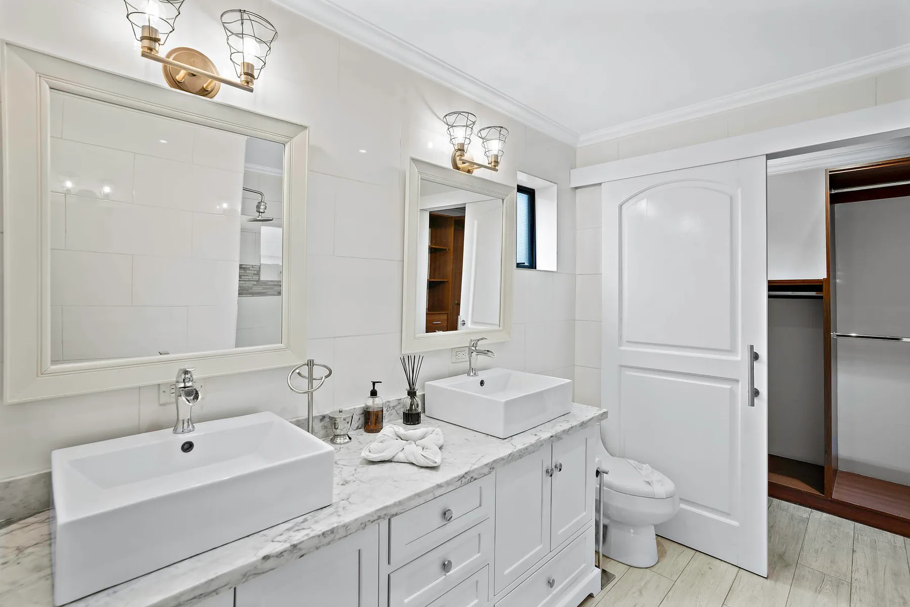 A bright bathroom with a long vanity, two sinks, and a partially open door.