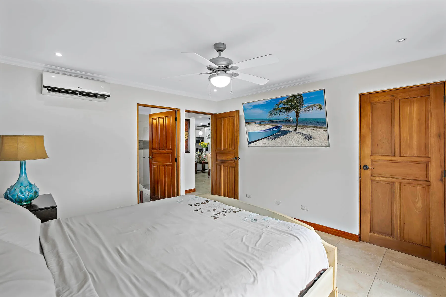 A bedroom with a bed, wooden doors, and a beach picture on the wall.