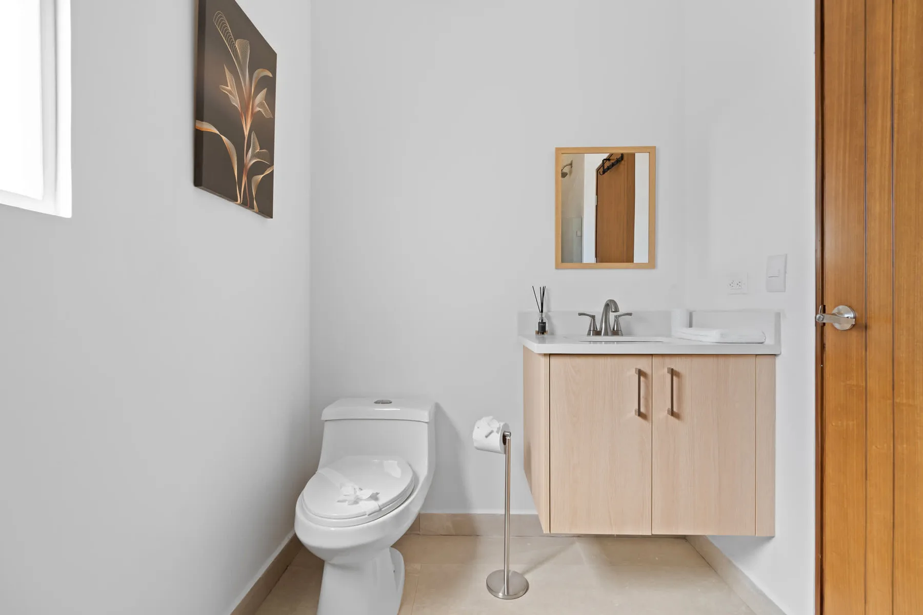 A bright bathroom with a toilet and a wooden vanity beneath a mirror.