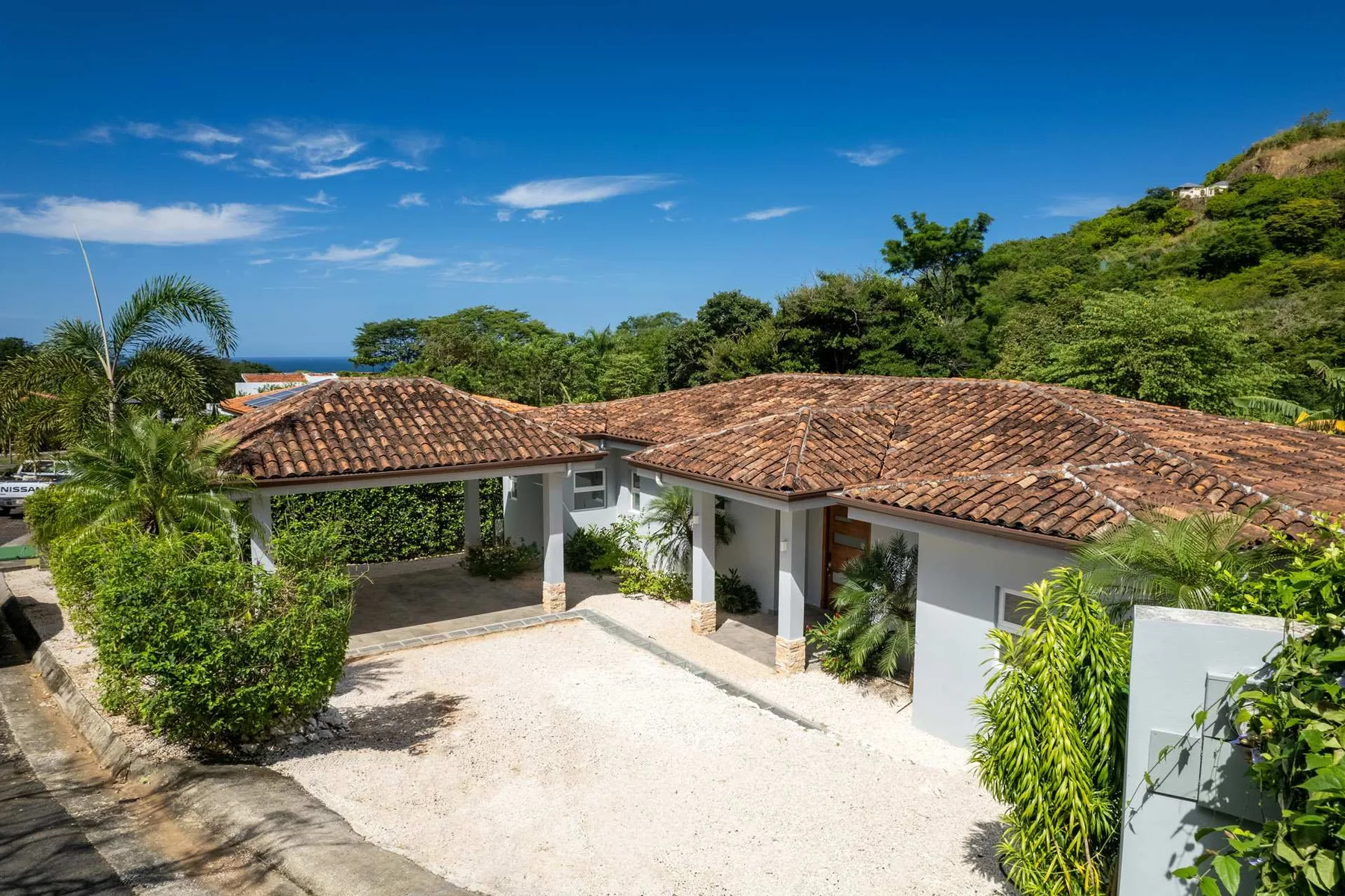 A low white building with a tiled roof sits amid greenery under a clear blue sky.