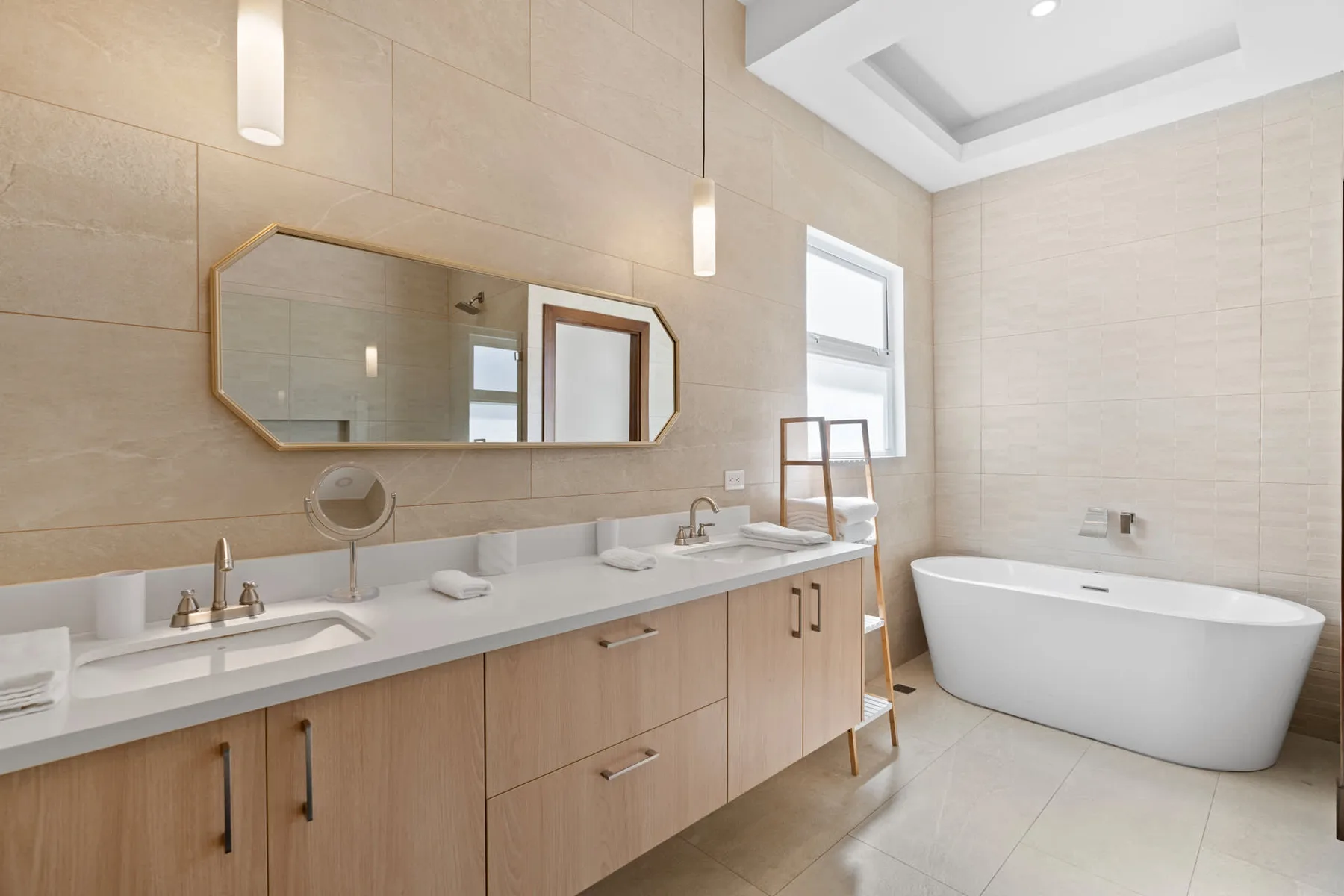 A bright bathroom with a long vanity, wide mirror, and freestanding bathtub.