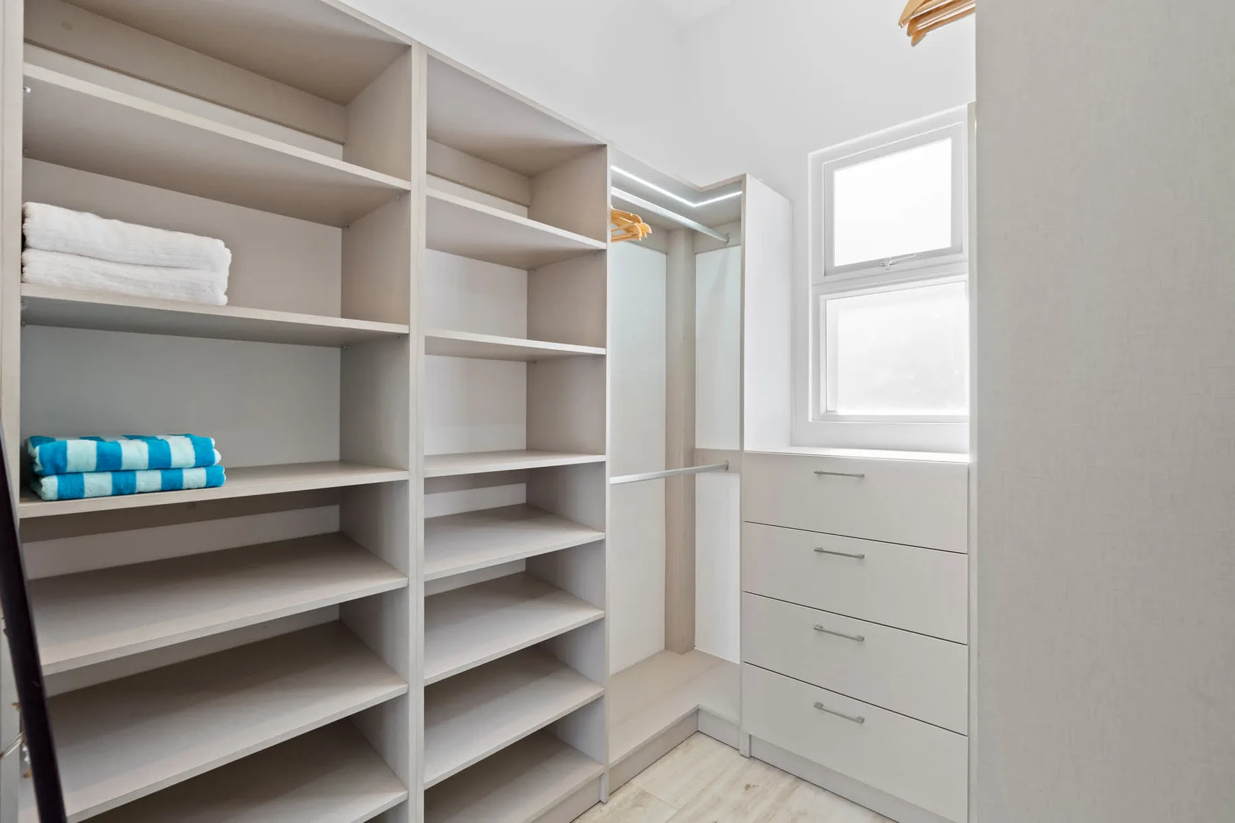A walk-in closet with open shelving, drawers, and folded towels.