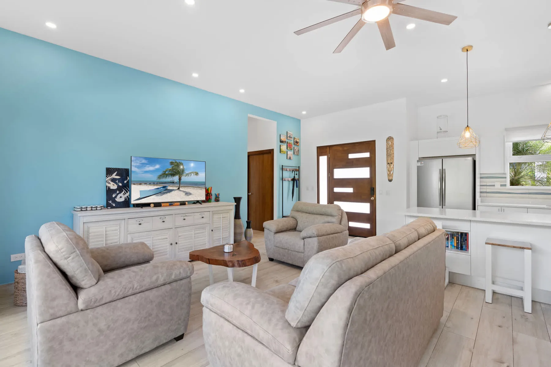 A bright living room with seating, a television, and a kitchen in the background.
