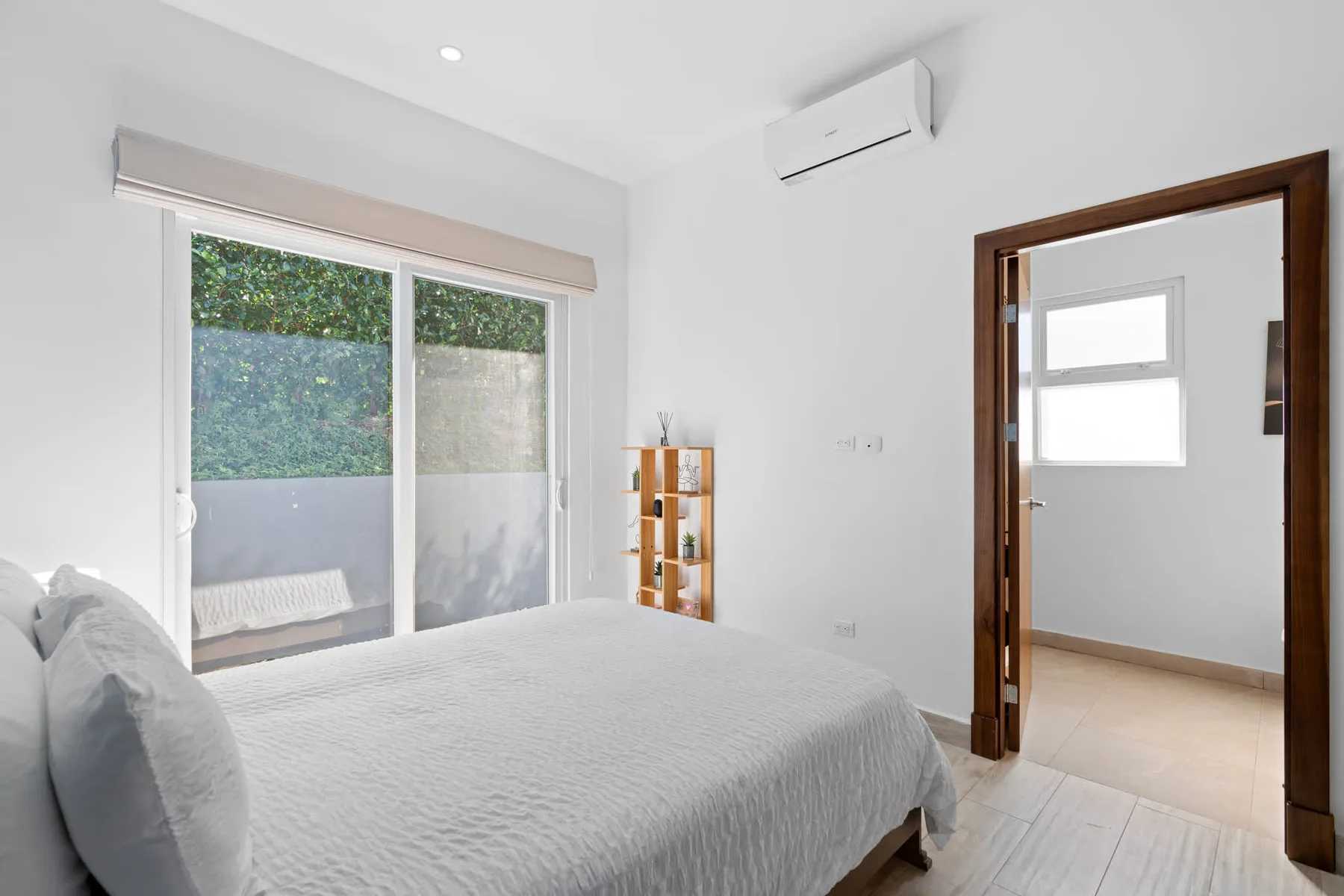 A bright bedroom with a bed beside sliding glass doors and a small shelf.