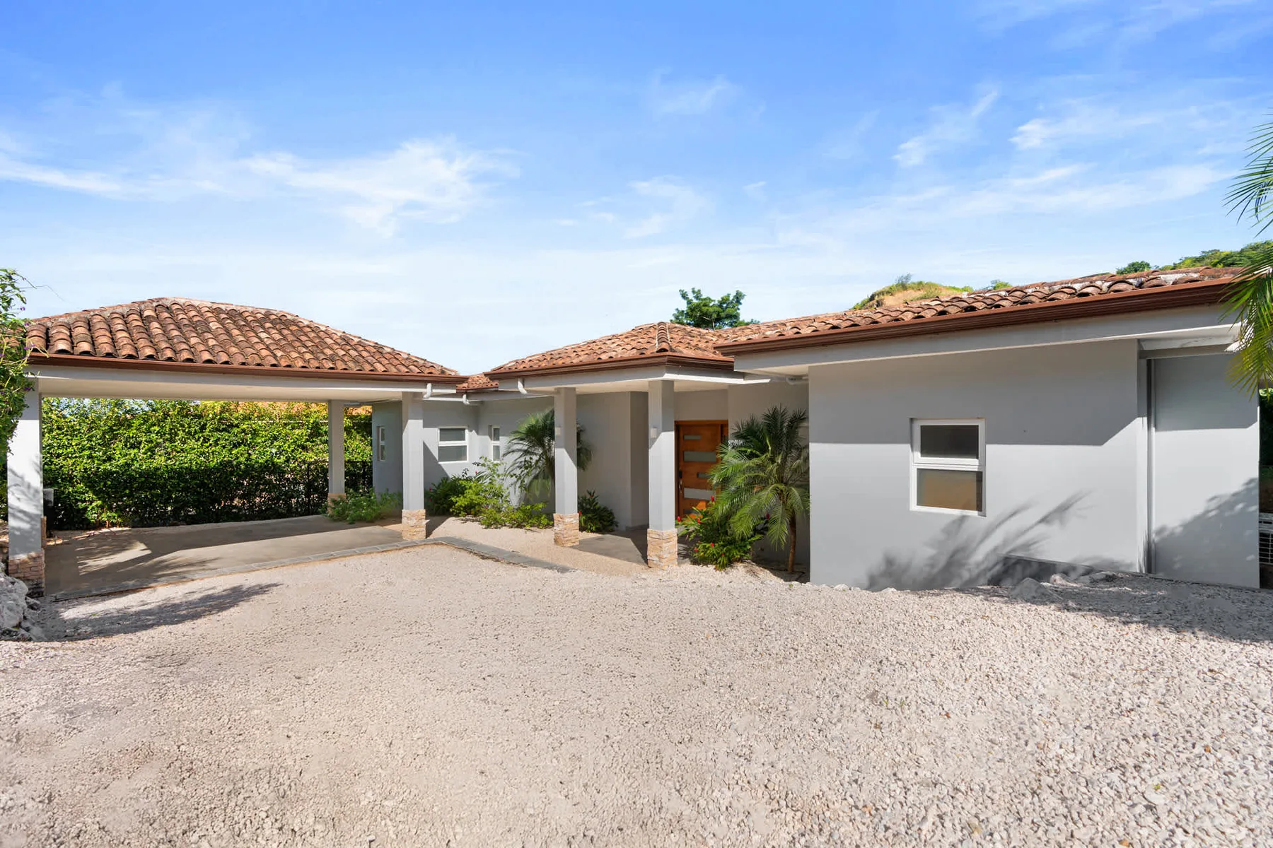 A single-story house with a tiled roof faces a broad gravel driveway.