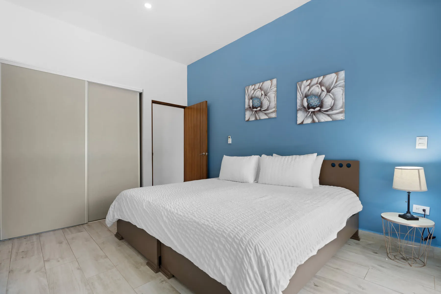 A bedroom with a neatly made bed and blue accent wall.