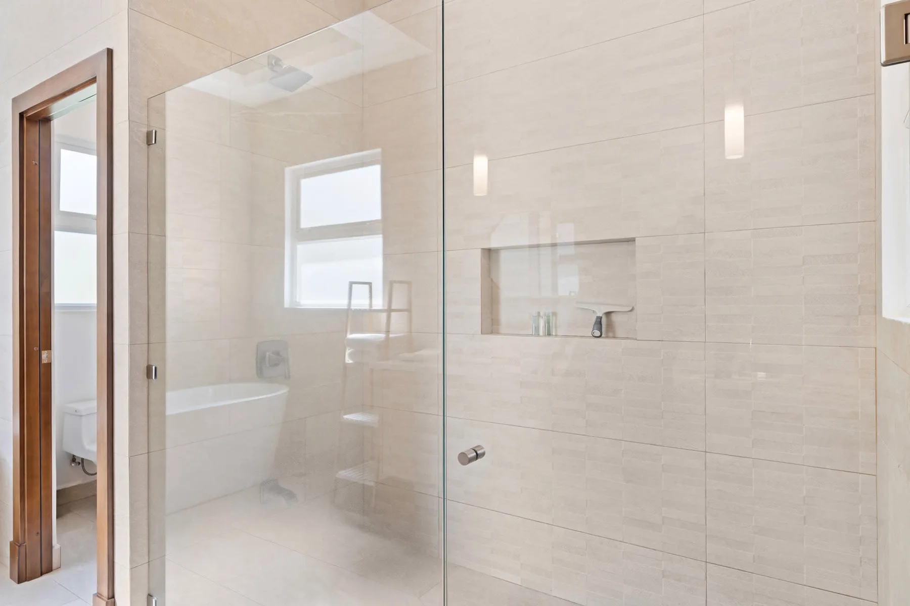 A bright tiled bathroom with a glass shower and a bathtub.