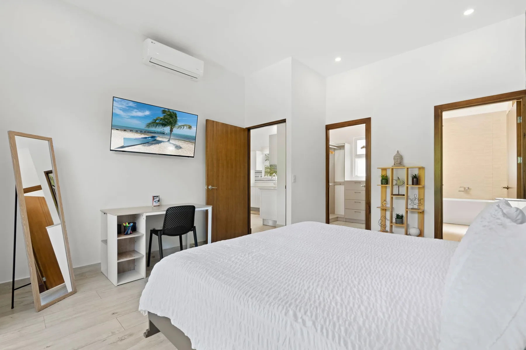 A bright bedroom with a bed, desk, and open doorways.