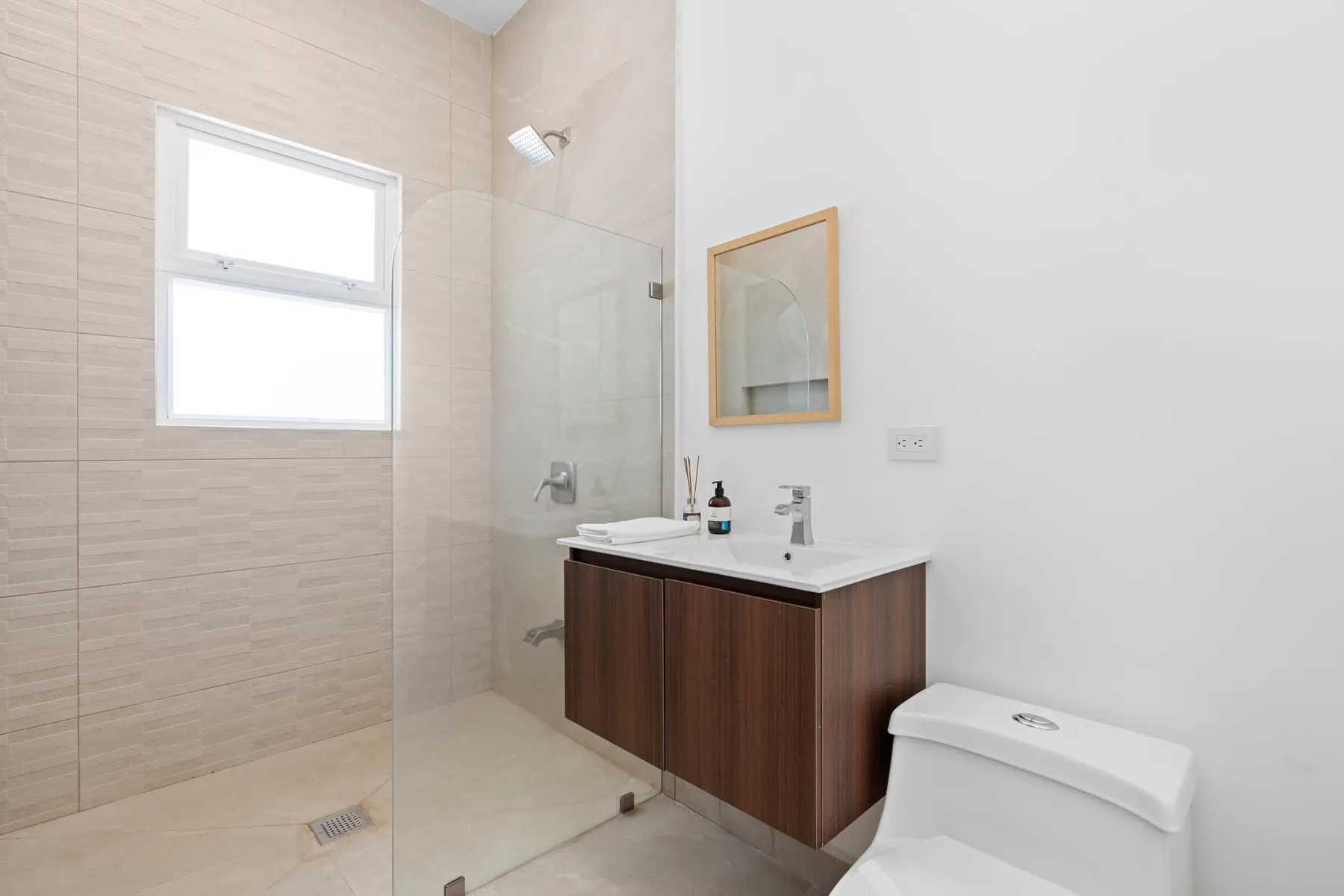 A bright bathroom with a glass shower, vanity, and toilet.